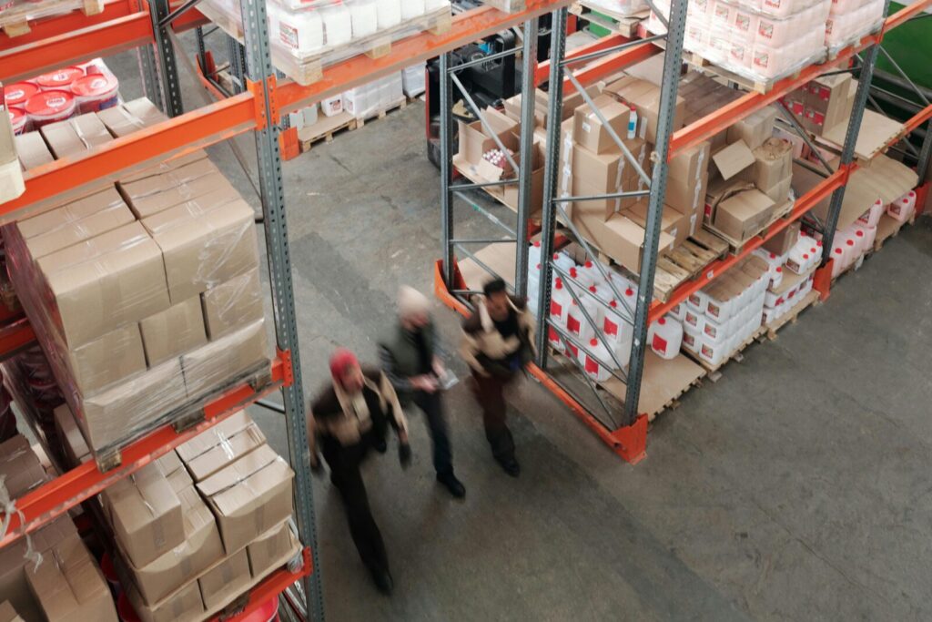 A high angle view of workers in motion in a busy warehouse with shelves full of boxes and packages.