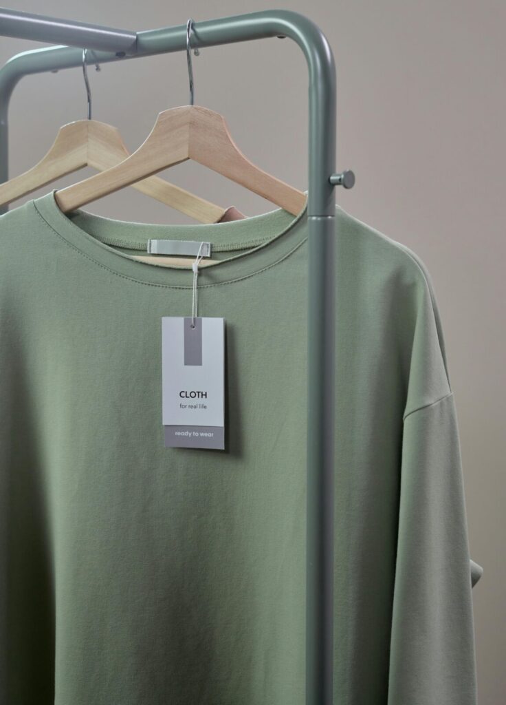 Close-up of a green shirt on a hanger with label tag on a minimalist clothing rack.